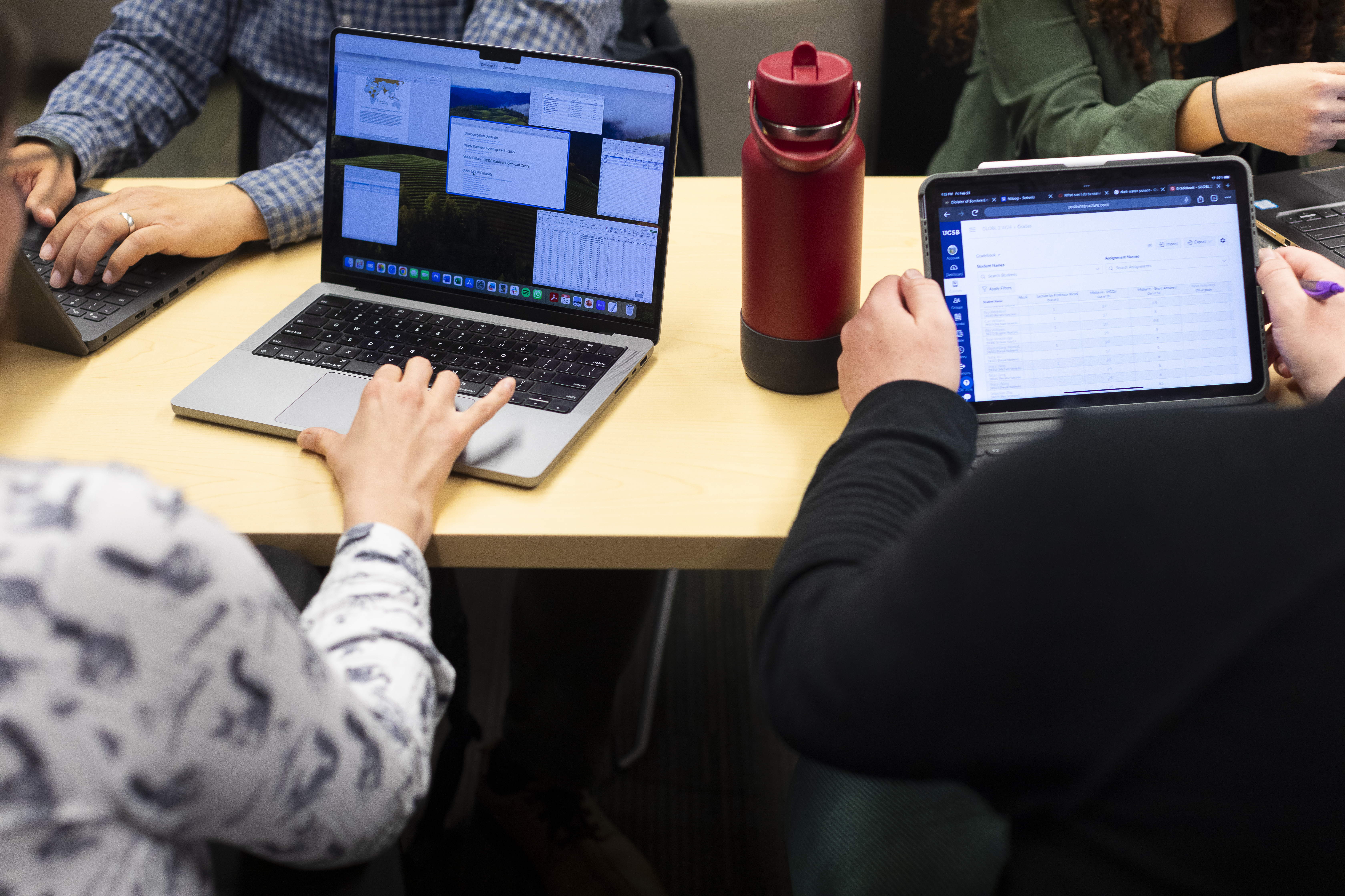 Two people sitting with backs to the camera. One with a computer, the other with a tablet. 